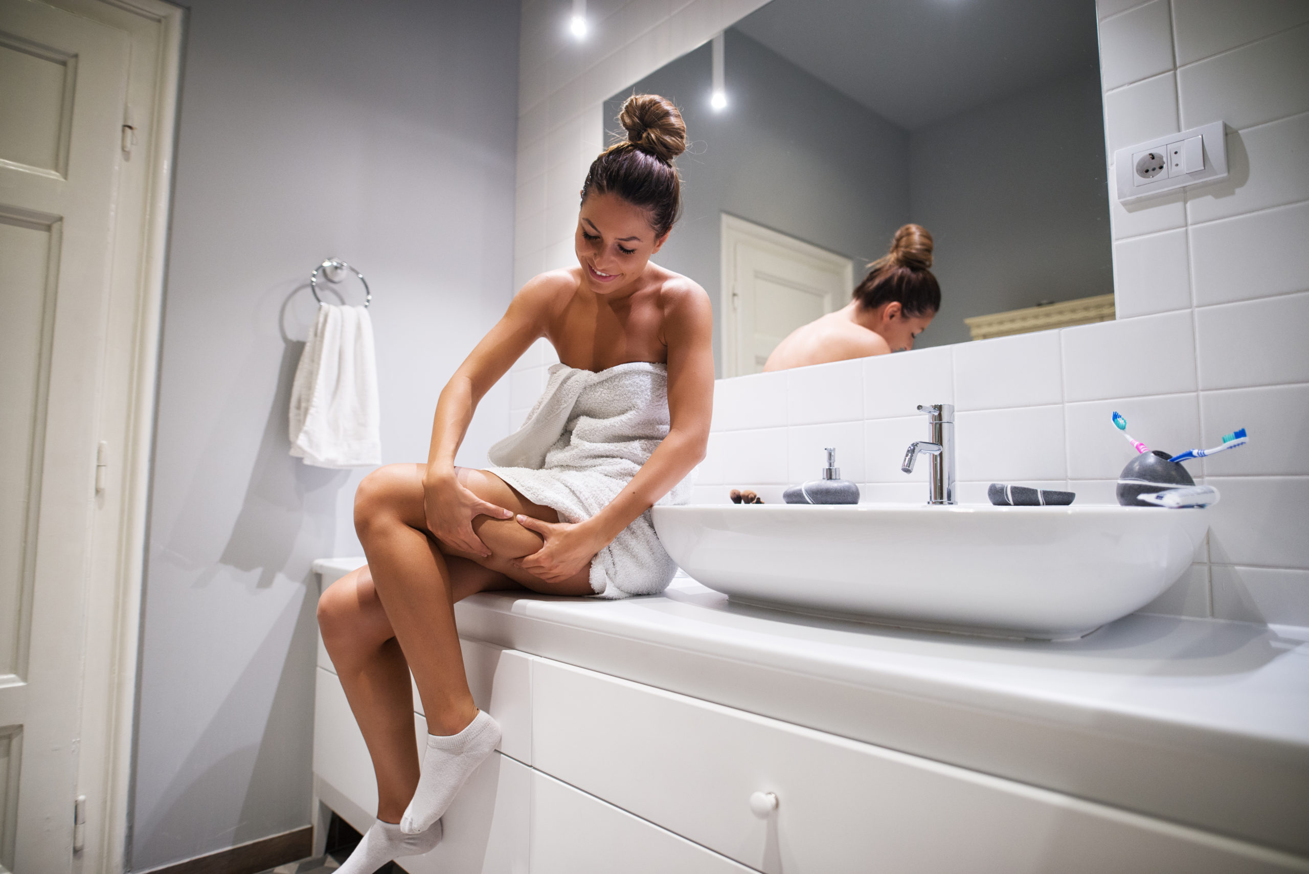 woman sitting on the bathroom counter in a towel, examining her leg before Cellulaze cellulite treatment