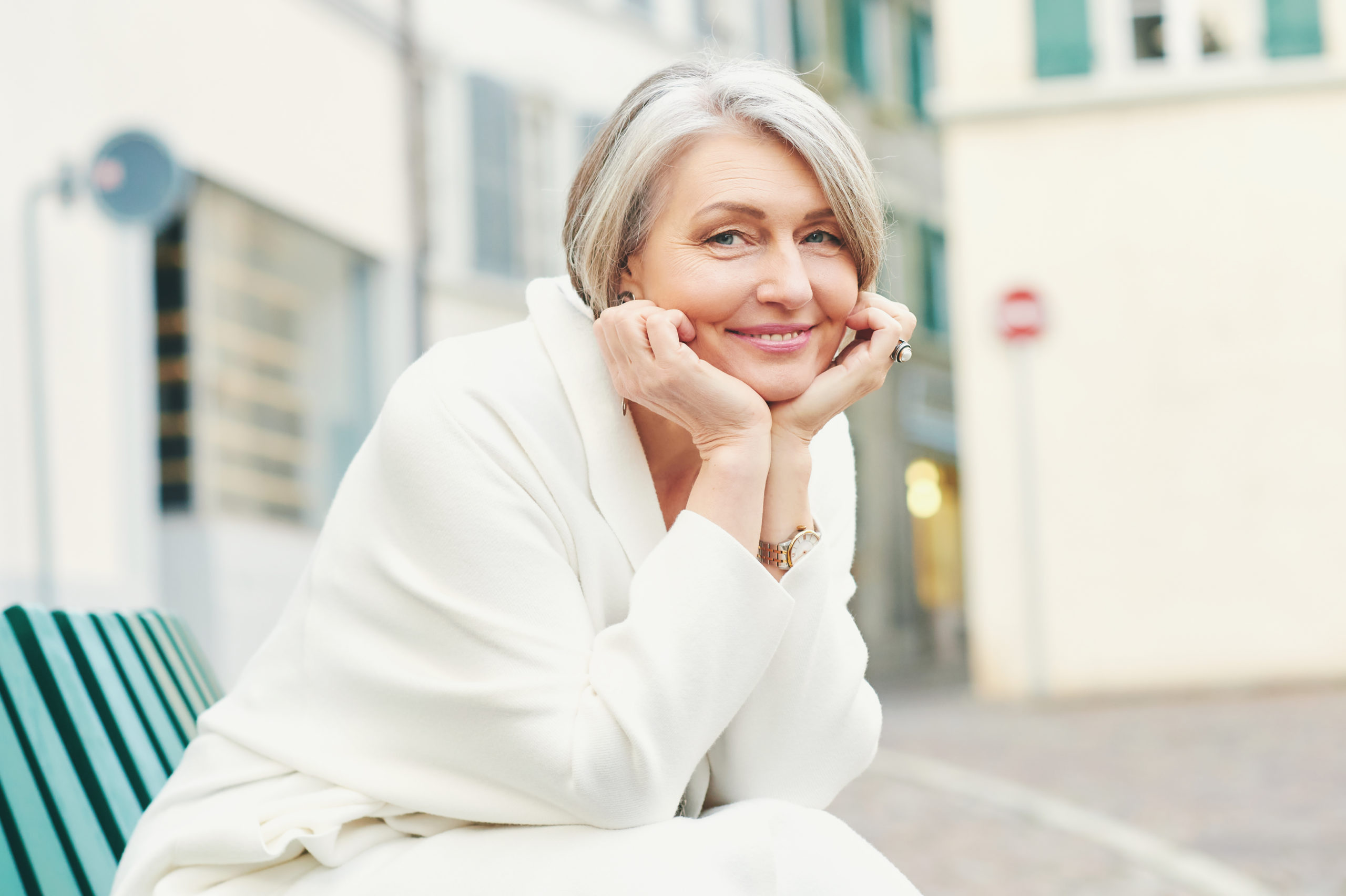 beautiful older woman sitting outside and smiling after receiving dermal fillers